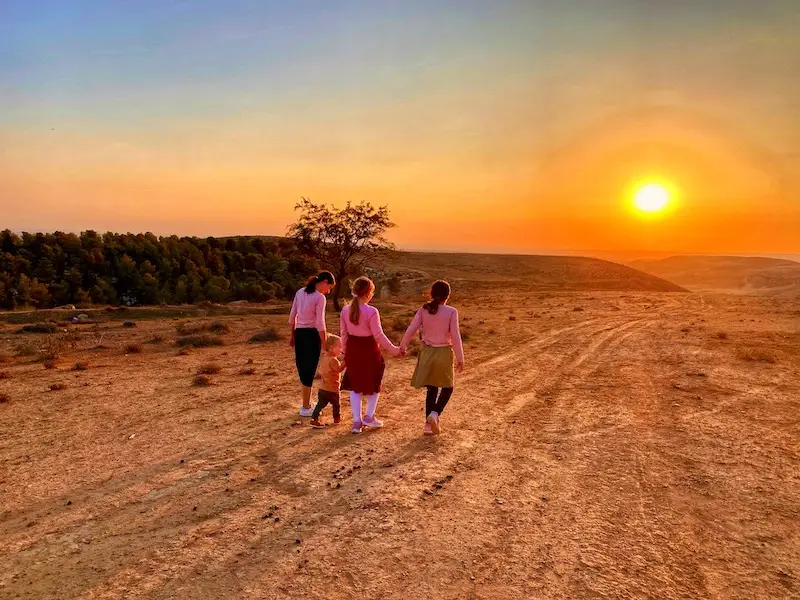 A family walking hand in hand toward the sunset over the Yatir Forest